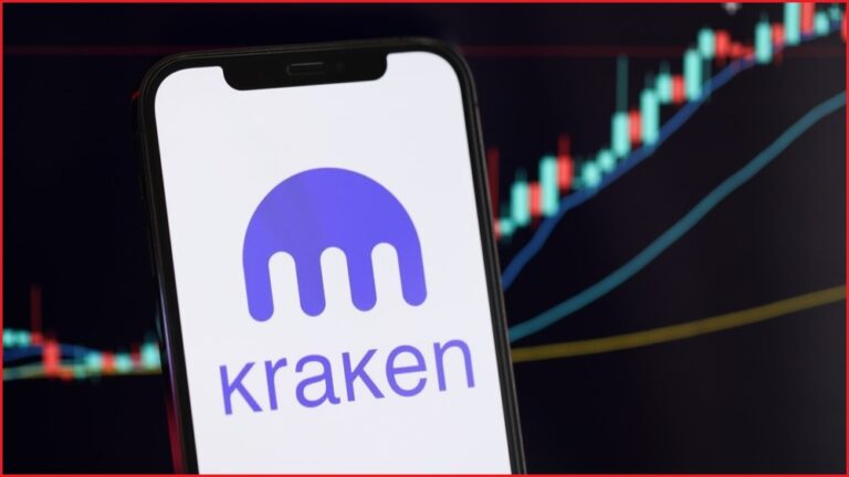 A close up of a smartphone displaying the Kraken cryptocurrency platform logo, with a crypto trading chart in the background.